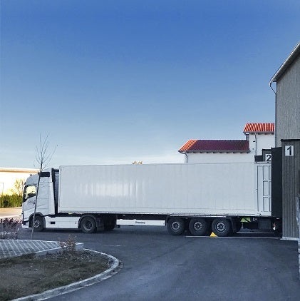 Lorry with a white trailer in front of a warehouse