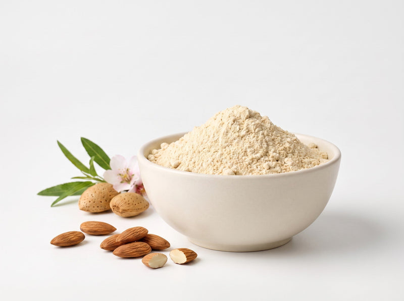 Light-coloured protein powder in a white bowl with almonds and almond blossoms