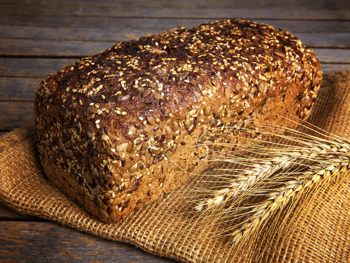 Vollkornbrot mit Körnern auf Jutetuch neben Weizenähren